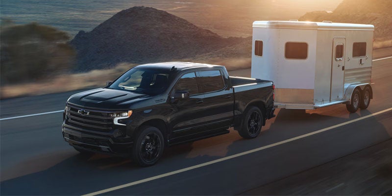 A Chevrolet Silverado 1500 towing a horse trailer on a rural road, showcasing its towing capability and rugged design.